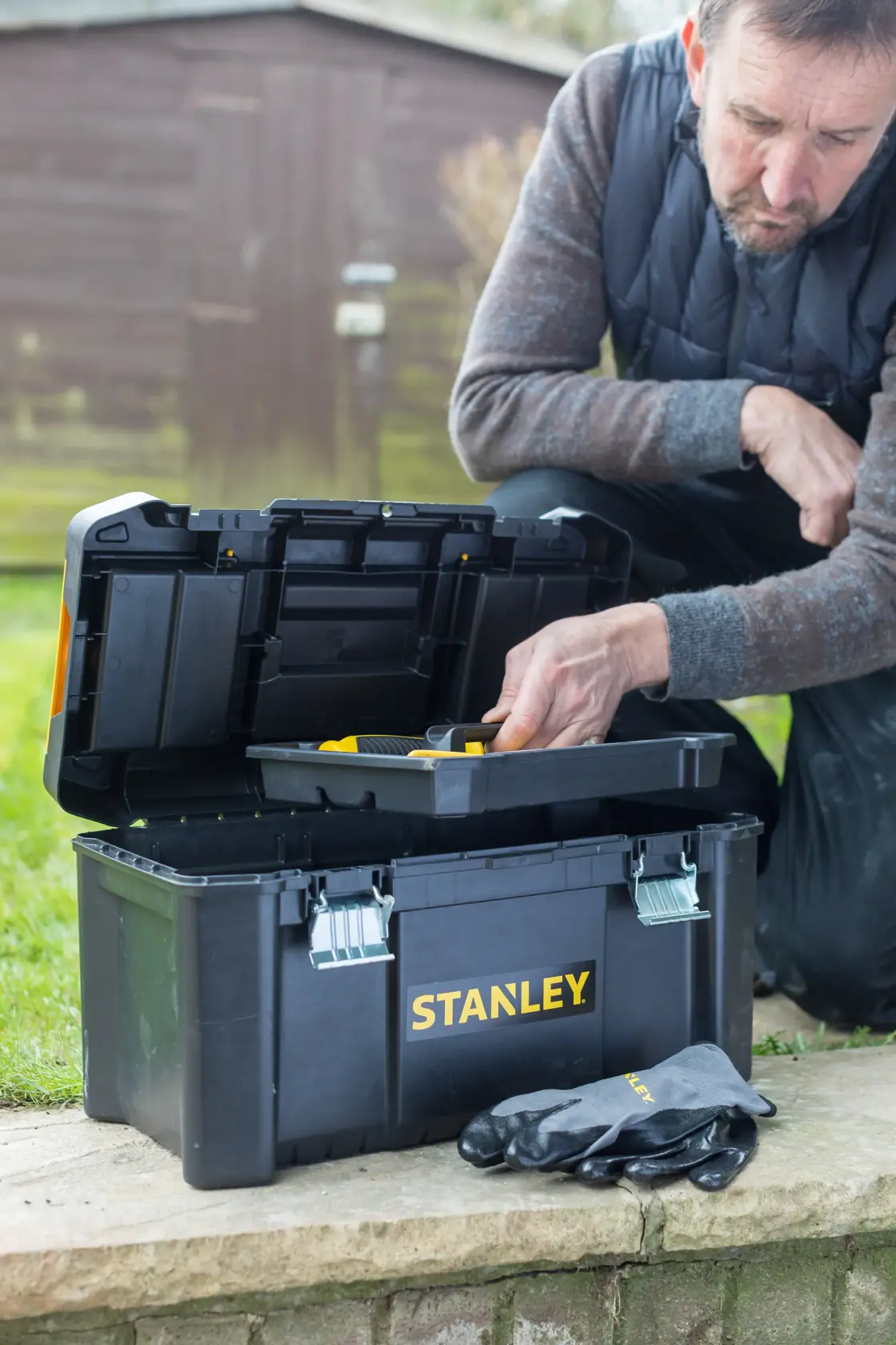 Foto des STANLEY STST1-75521 Werkzeugkastens im Freien, Deckel offen mit Einsatz, Handschuhe vorne.