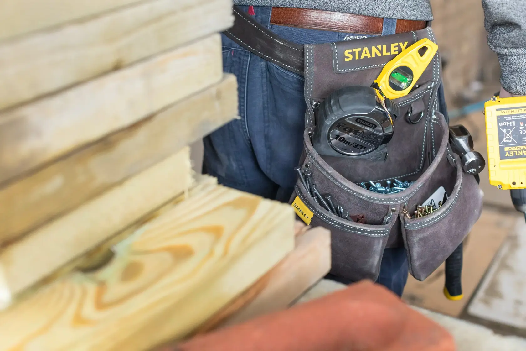 Foto des STANLEY STST1-80116 Werkzeuggürtels mit Werkzeugen und Zubehör, getragen neben Holzplanken.